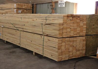 Stacks of treated lumber in a warehouse with labels indicating sizes.