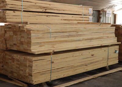 Stacks of treated lumber in a warehouse with labels indicating sizes.