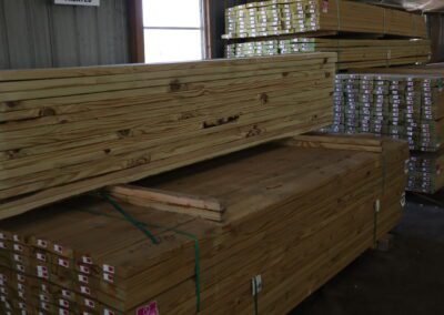 Stacks of treated lumber in a warehouse with labels indicating sizes.