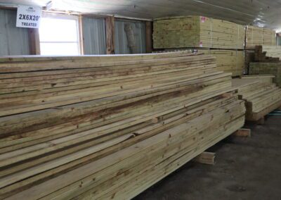 Stacks of treated lumber in a warehouse with labels indicating sizes.