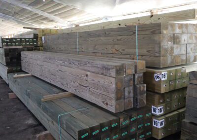 Stacks of treated lumber in a warehouse with labels indicating sizes.