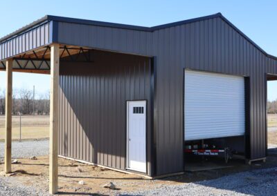 A gray metal shed with a large roll-up door and an attached open carport.