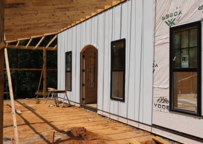 New construction house with exposed wooden framework and wrapped insulation, featuring windows and a door.