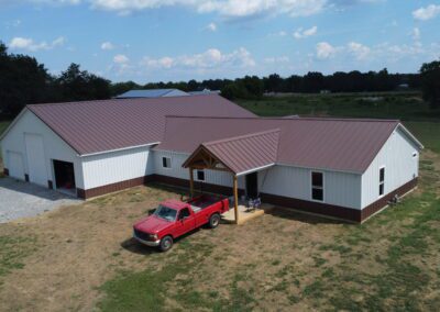 Aerial view of two barn-style buildings with metal roofs and a red pickup truck in front.