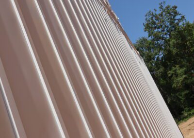 White corrugated metal siding on a building with trees and a blue sky in the background.