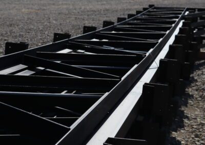 Rows of stacked black metal beams in an outdoor storage yard.