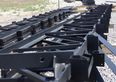 Rows of stacked black metal beams in an outdoor storage yard.